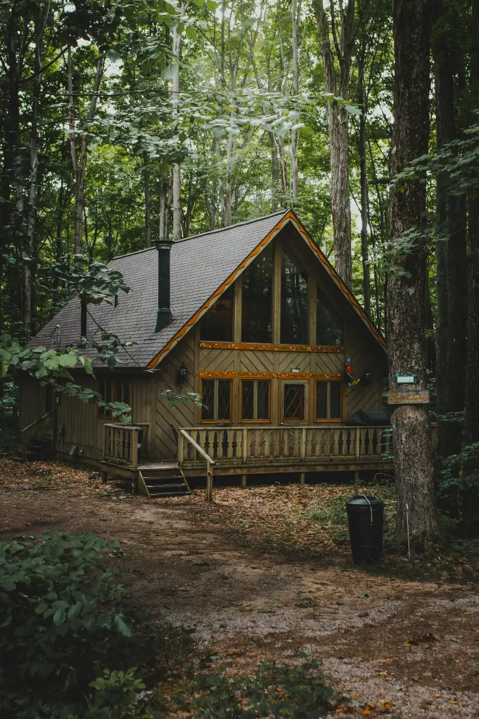A wooden cabin with a large porch, set among tall trees.