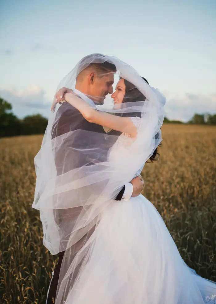A couple embracing in a wheat field, the bride's veil lifted by the wind.