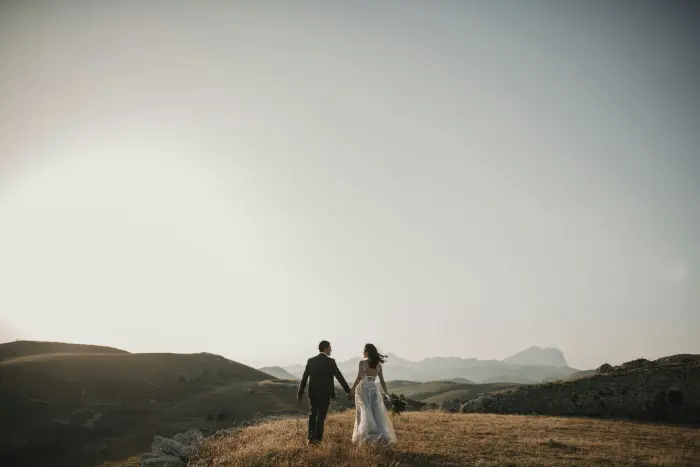 A couple walking hand in hand across rolling hills.