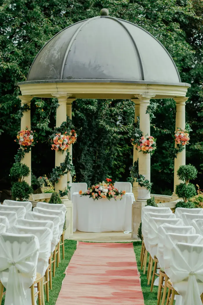 A white colonnade wrapped in flowers and greenery, set up for a ceremony.