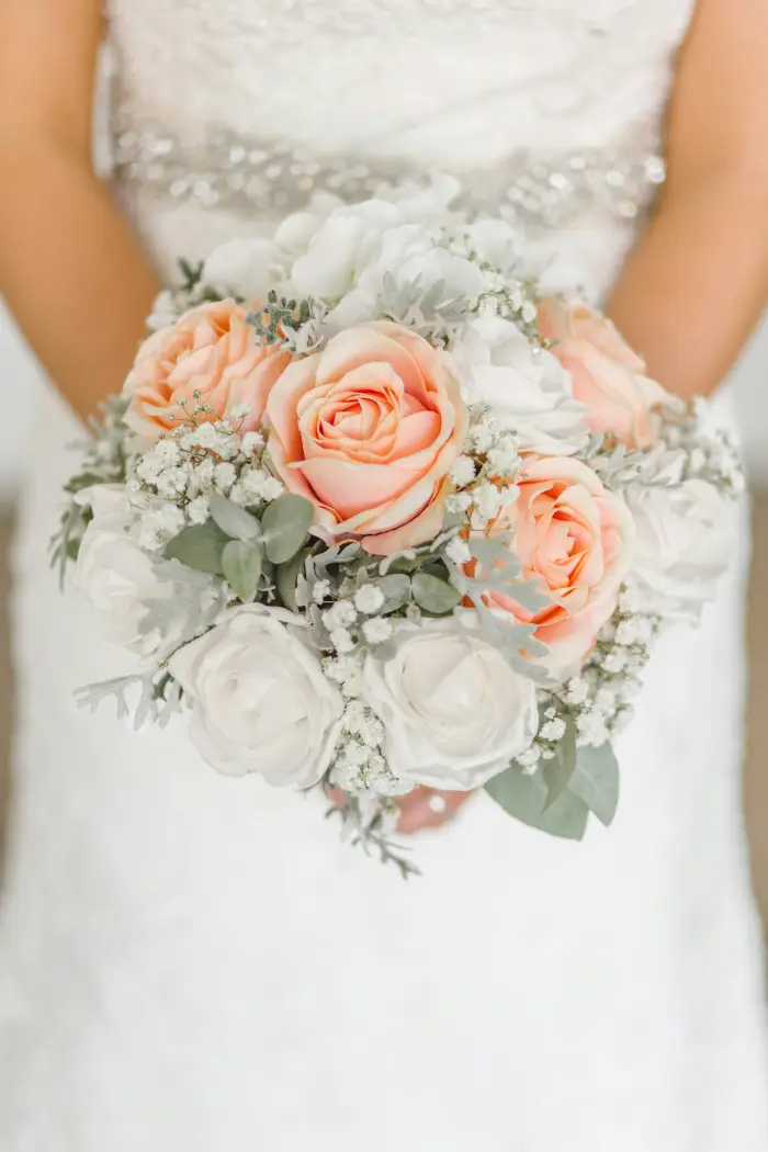 A bride holding a bouquet of peach roses and white flowers.