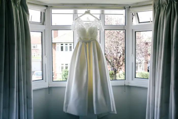 A wedding dress hanging in a bright bay window.